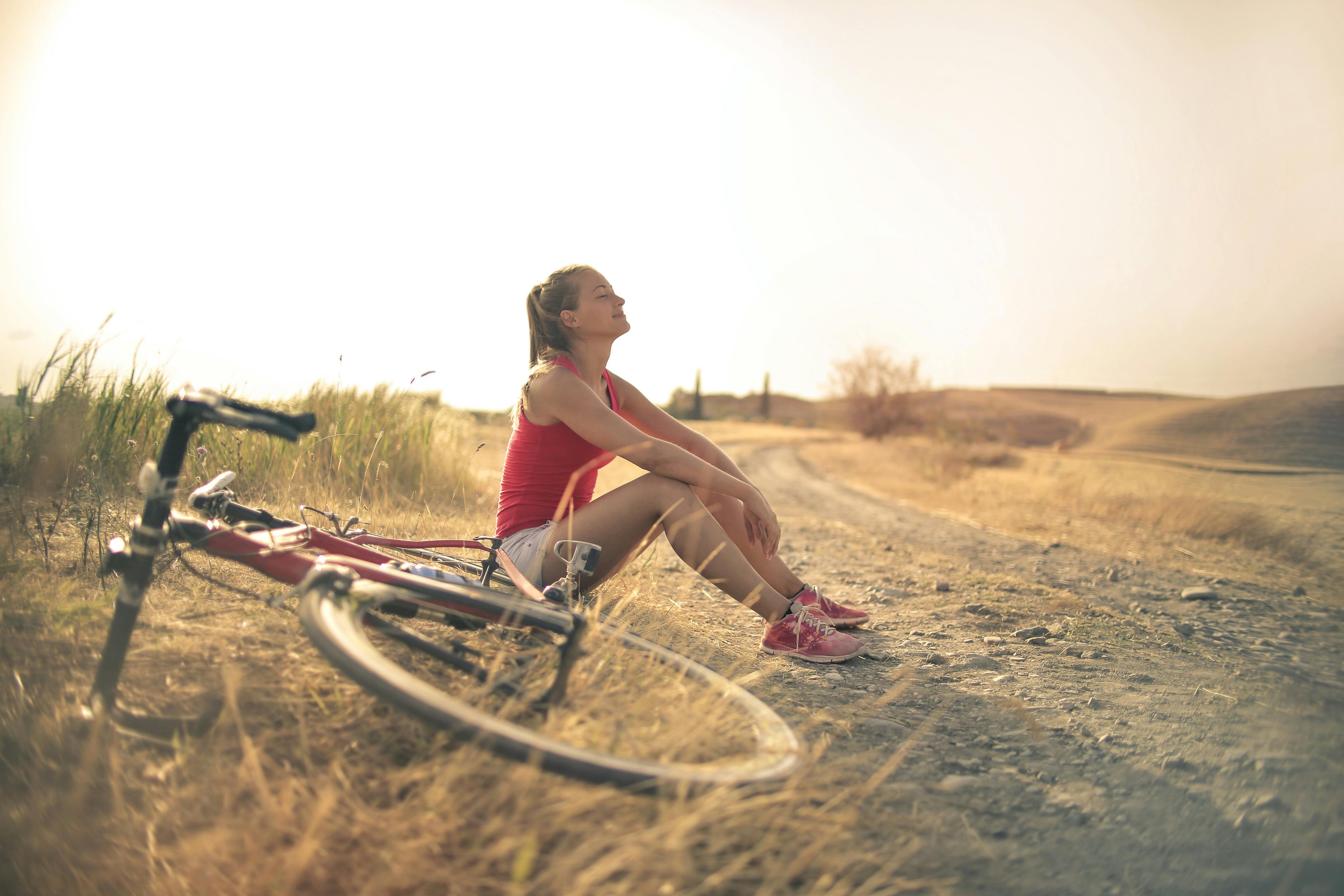 hero image of a woman sitting on a dirt path with a bicycle deeply breathing, surrounded by grass and a sunset